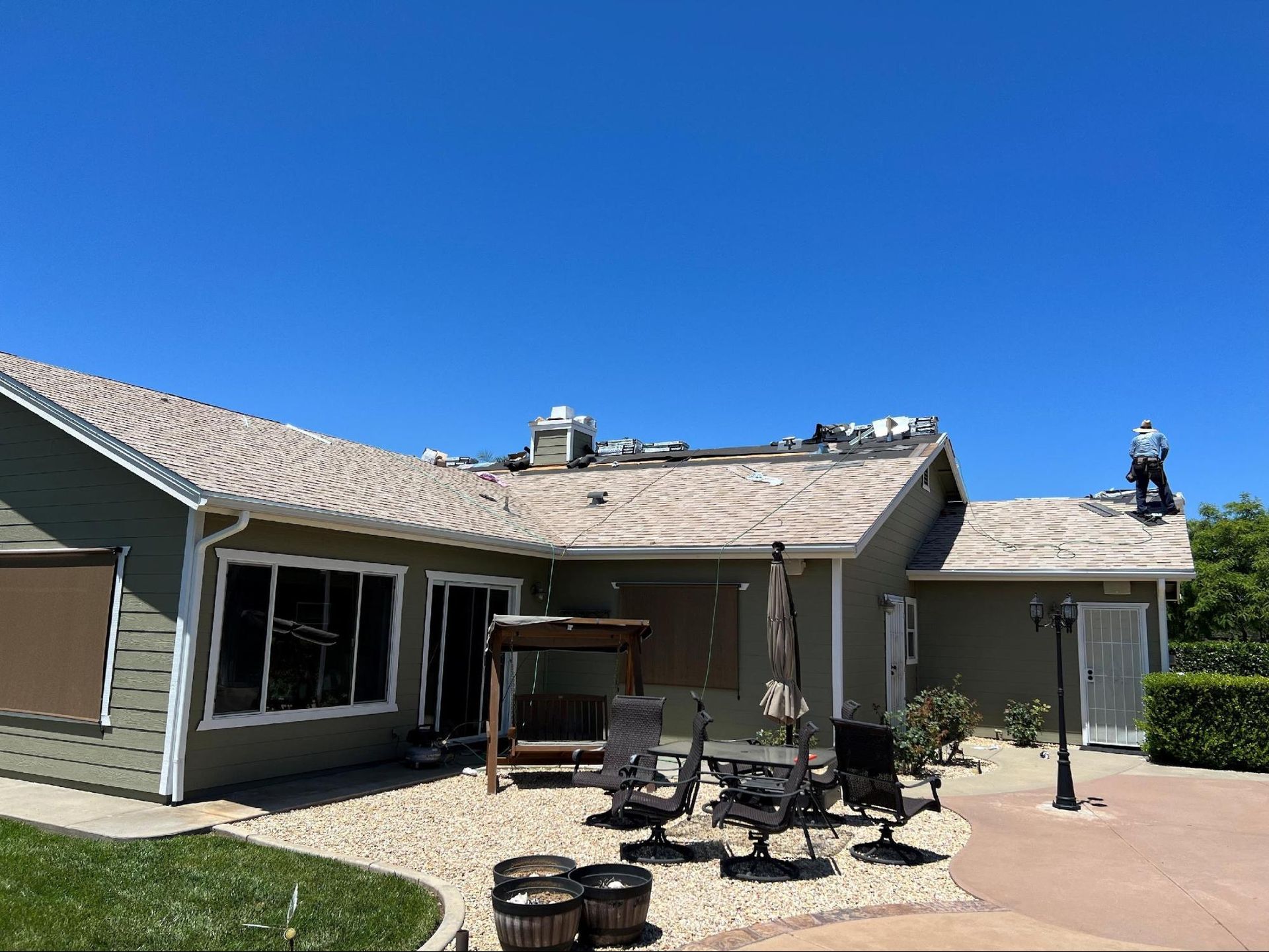 House with roof damage; a worker on the roof under a clear, blue sky.