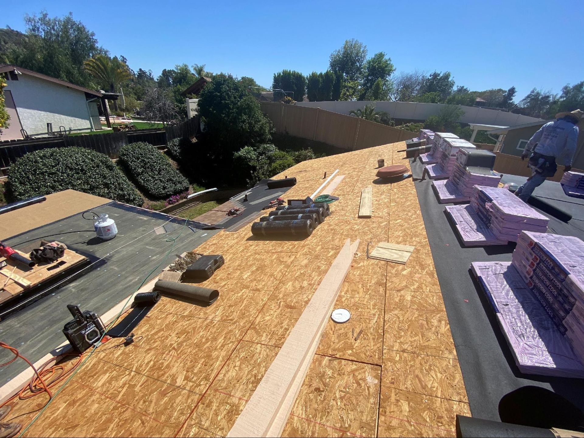 Construction worker on a rooftop, laying roofing materials in a sunny outdoor setting.