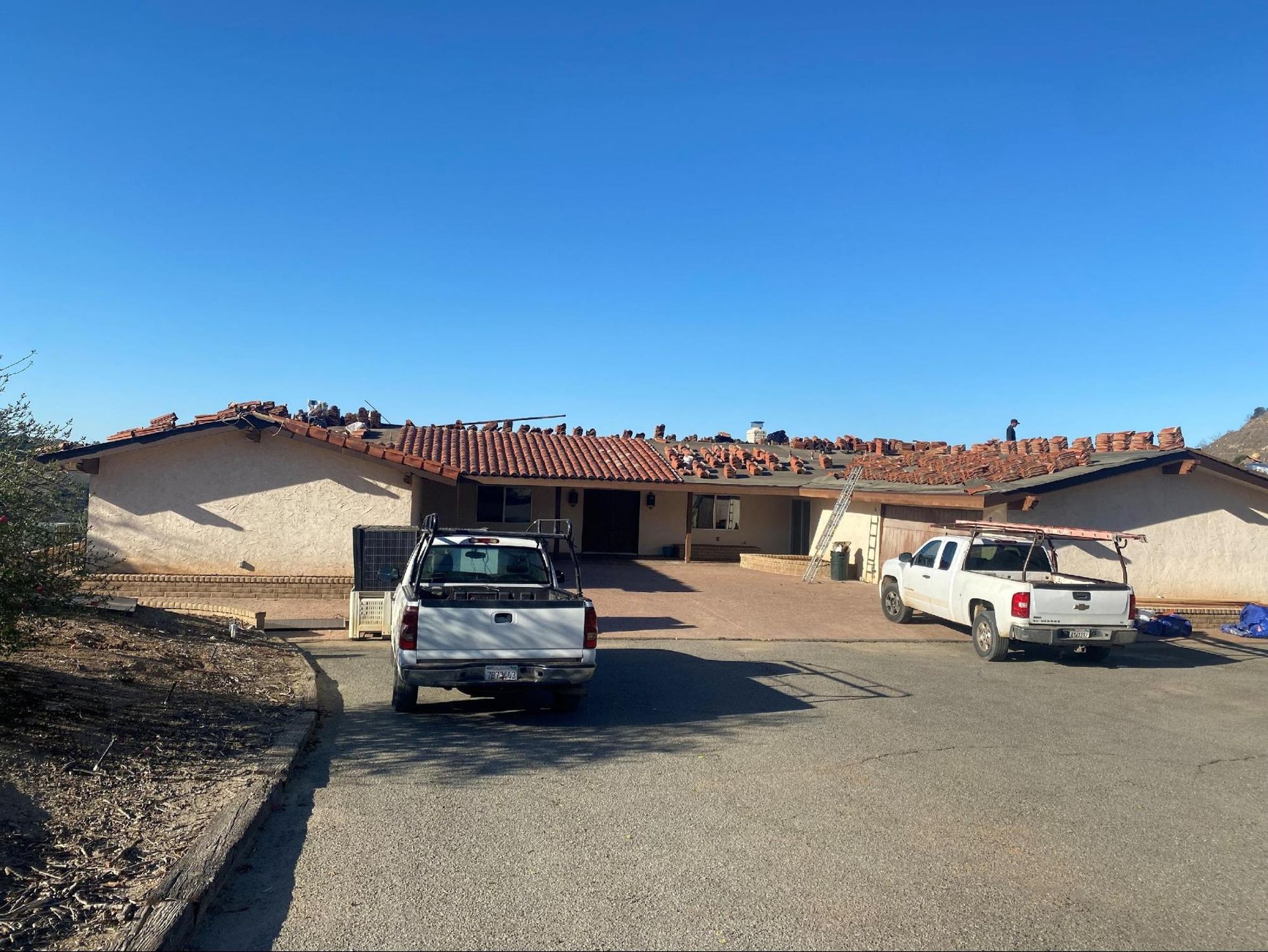 A house with workers on the roof, two trucks parked in the driveway under a clear blue sky.