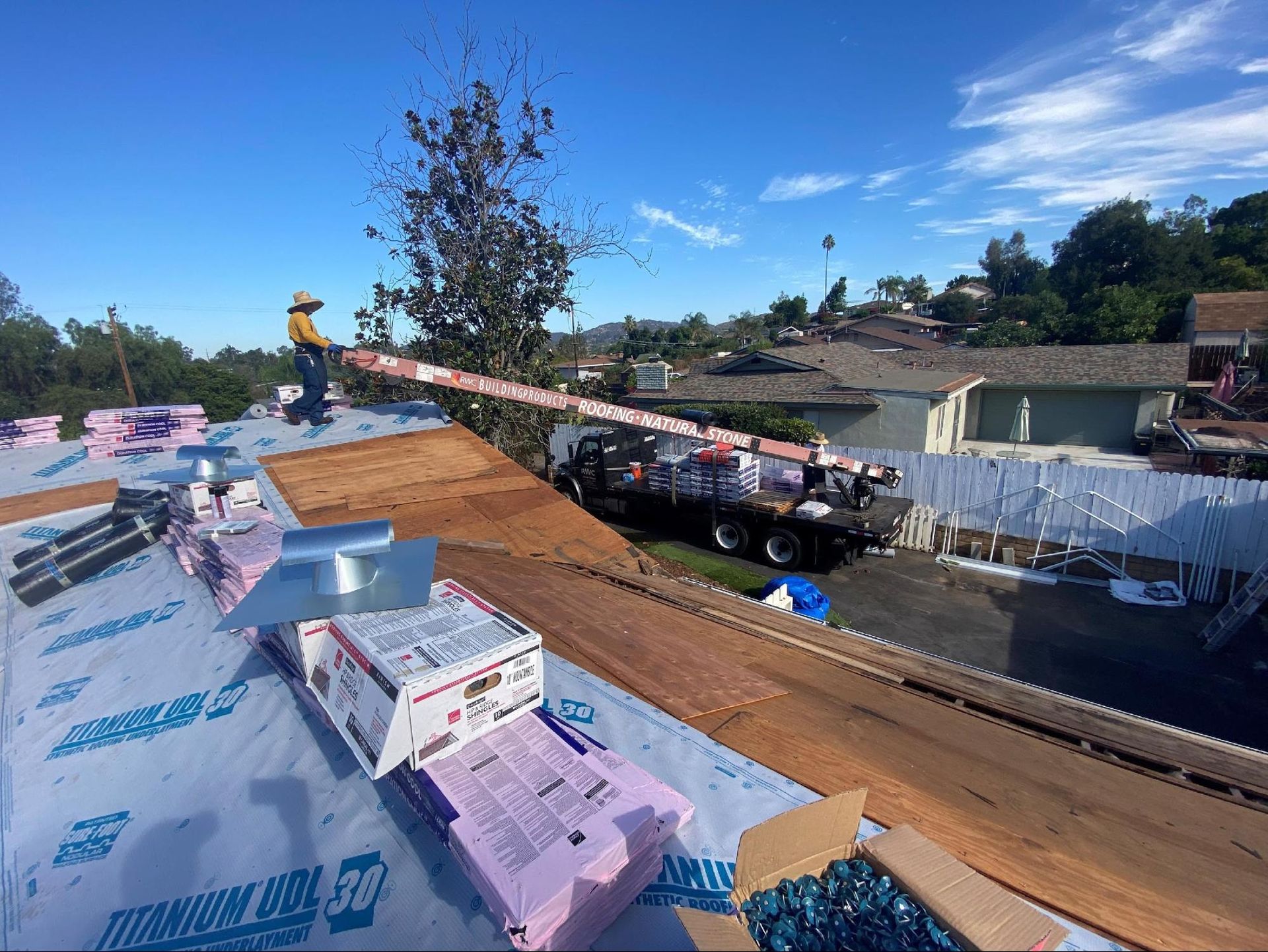 Roofer on a roof, using an aerial lift to access materials, on a sunny day.