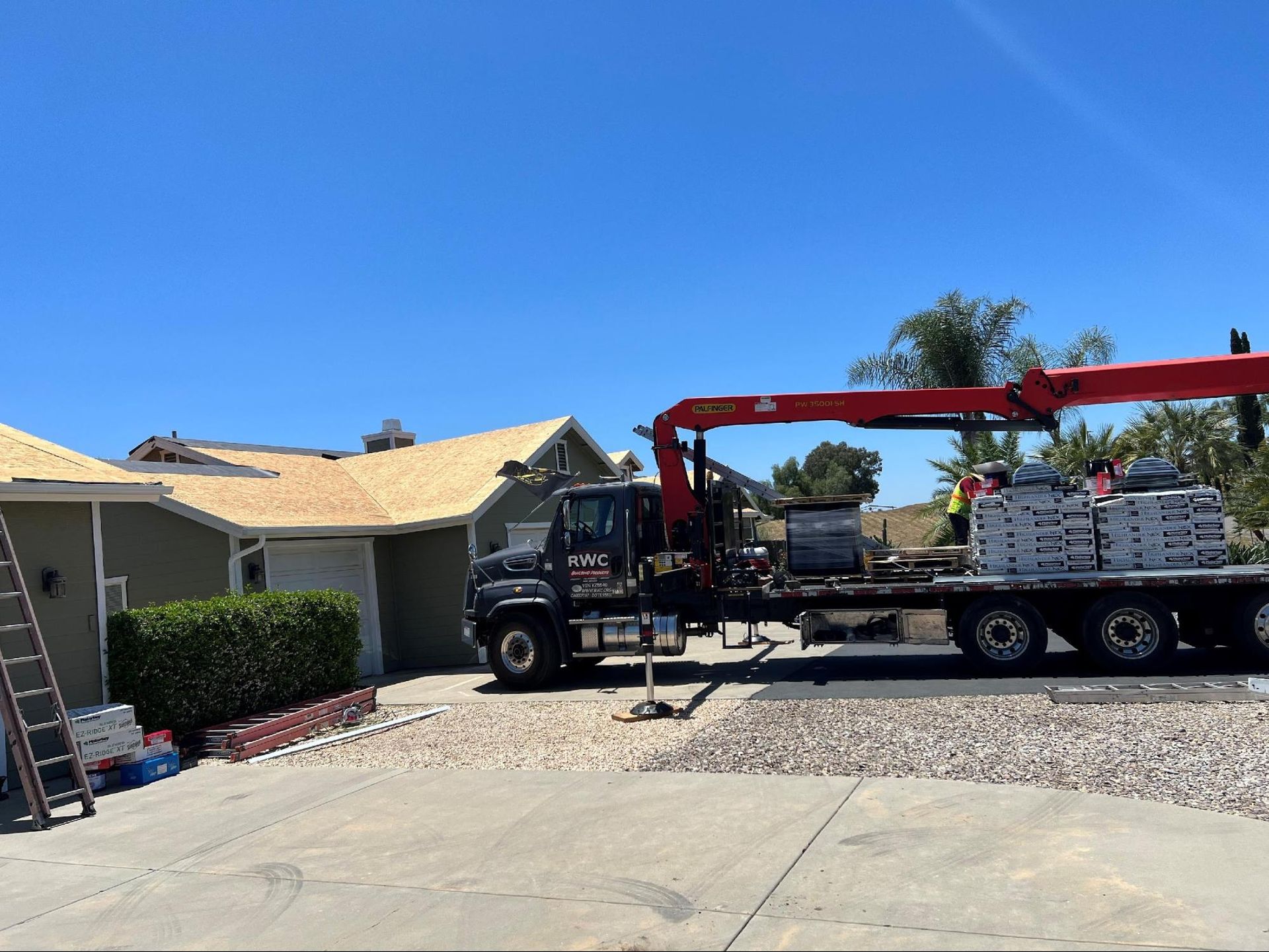 A roofing truck crane unloading shingles near a home. Blue sky overhead.