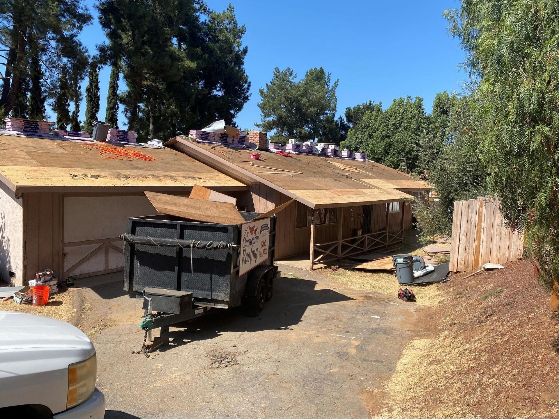 Two buildings under roof repair; a trailer loaded with debris is in the foreground, sunny day.