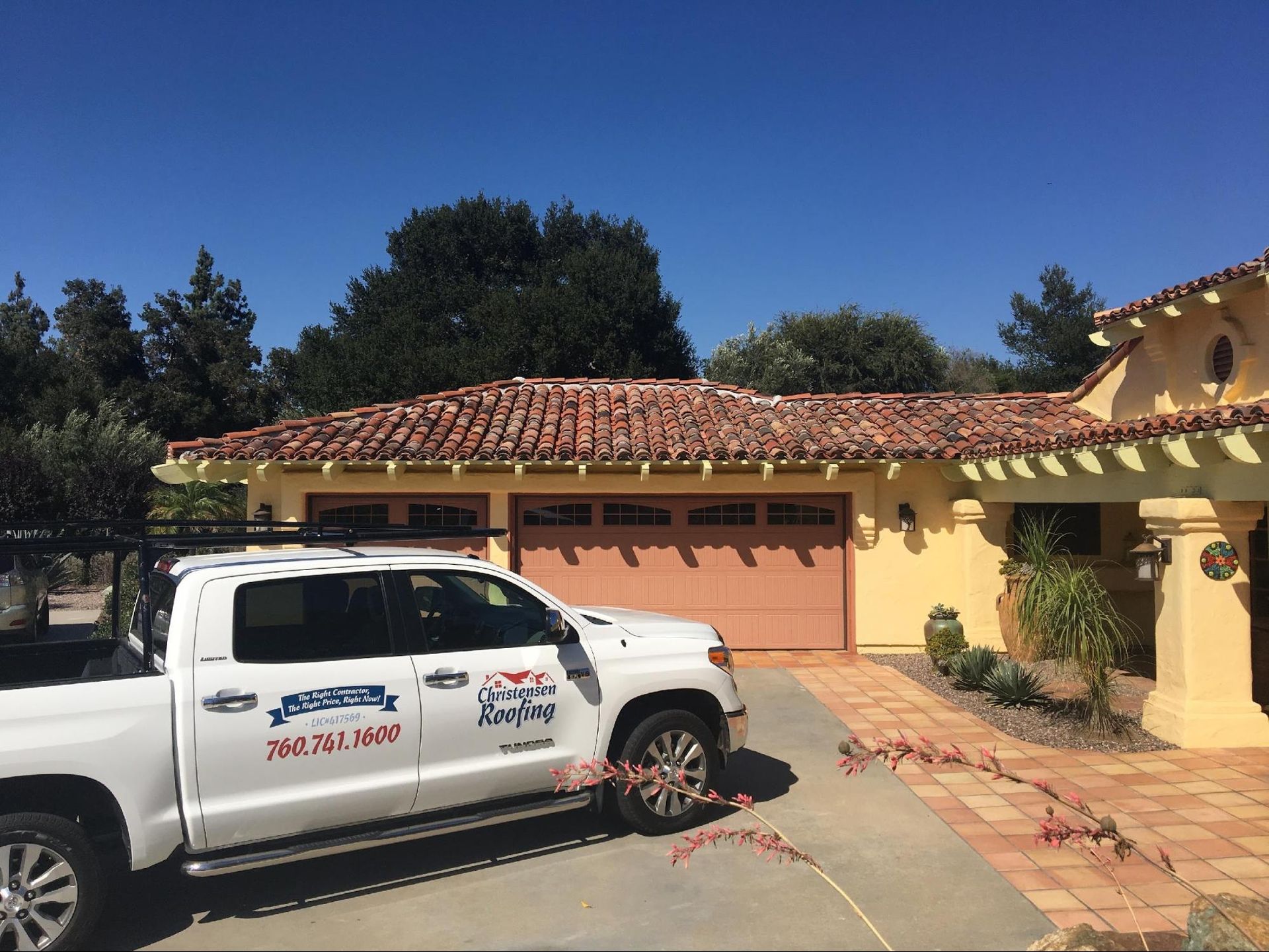 White truck with roofing logo parked in front of a tan house with a red tile roof.