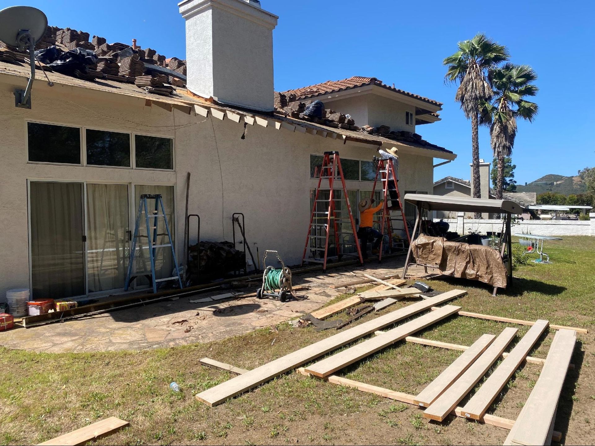 Exterior view of a house under construction, with workers on ladders and exposed roof.
