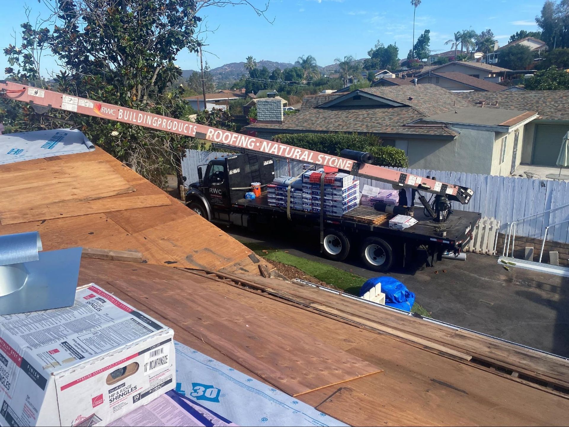 Roofing truck with extended boom delivering shingles to a roof. Sunny day.