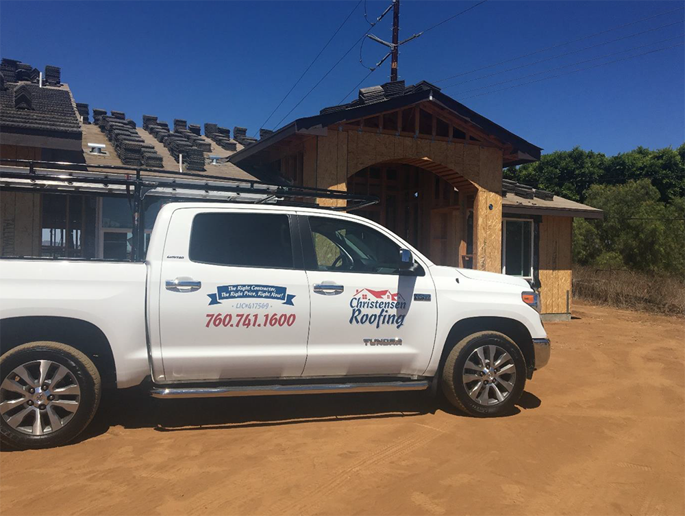 White roofing truck parked at a construction site on a sunny day.