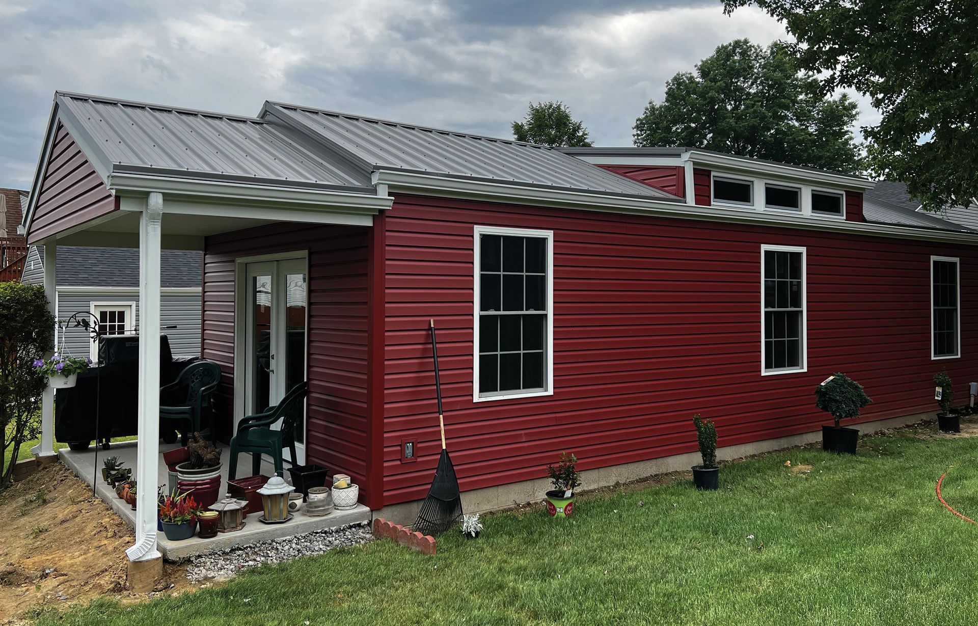 a red house with a porch and a metal roof is sitting on top of a lush green field