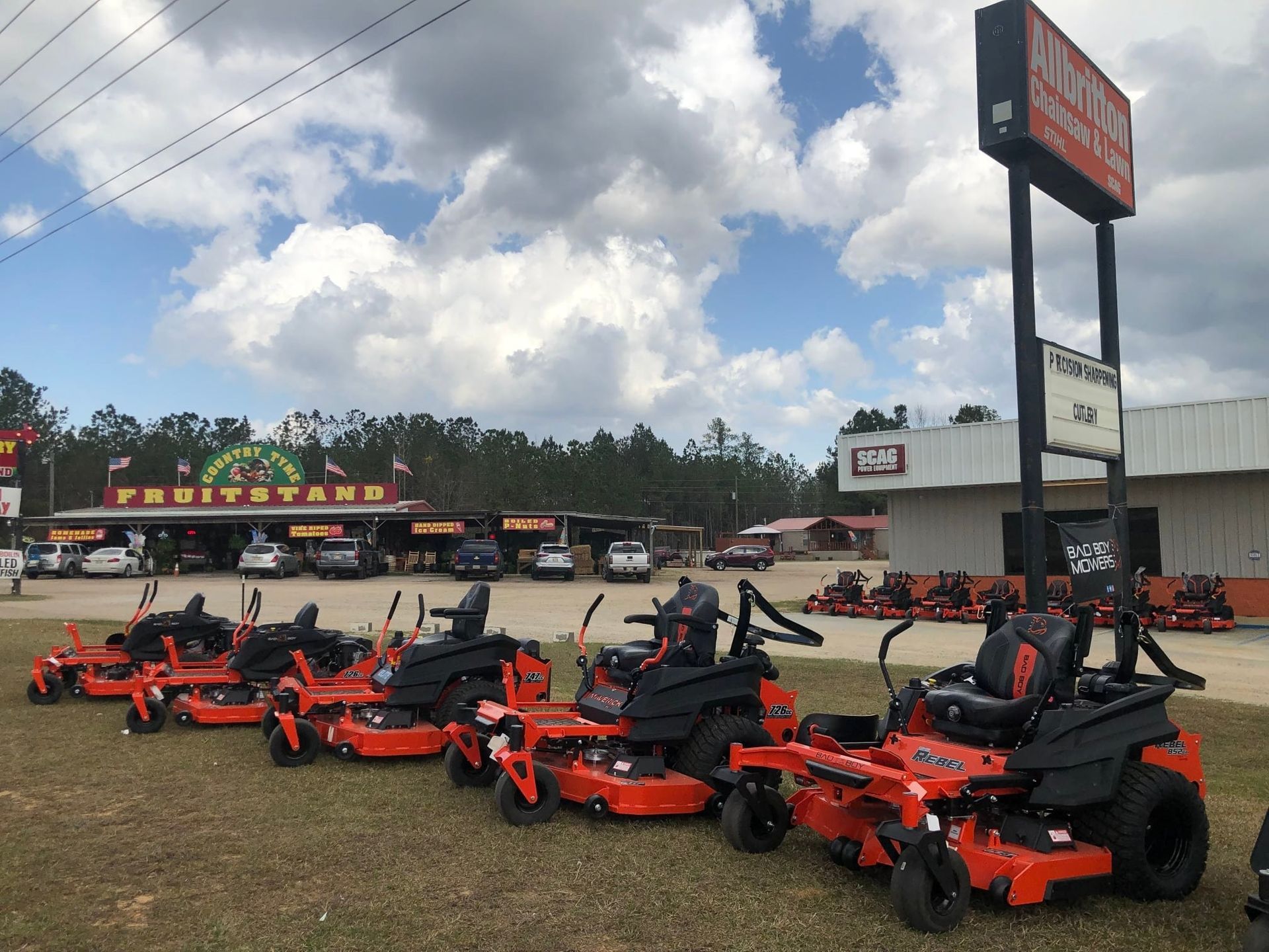 A row of orange zero-turn mowers in front of a lawn equipment store under a cloudy sky.