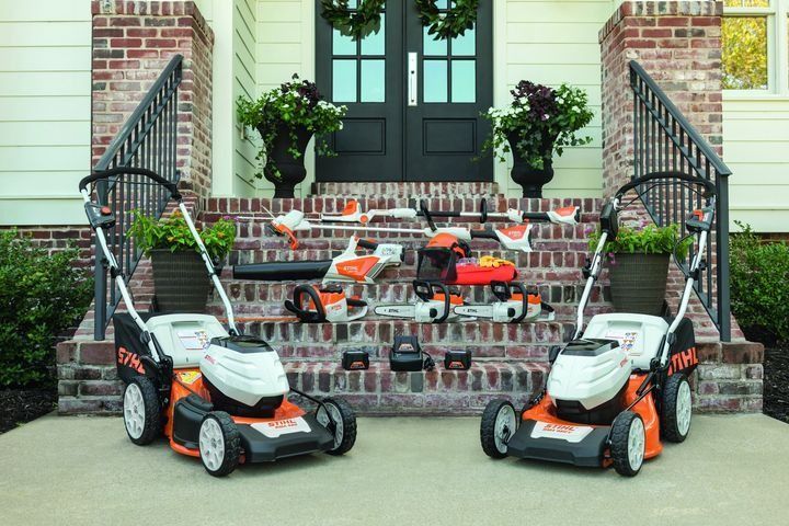 Two orange and white lawnmowers with other Stihl tools on steps in front of a house.