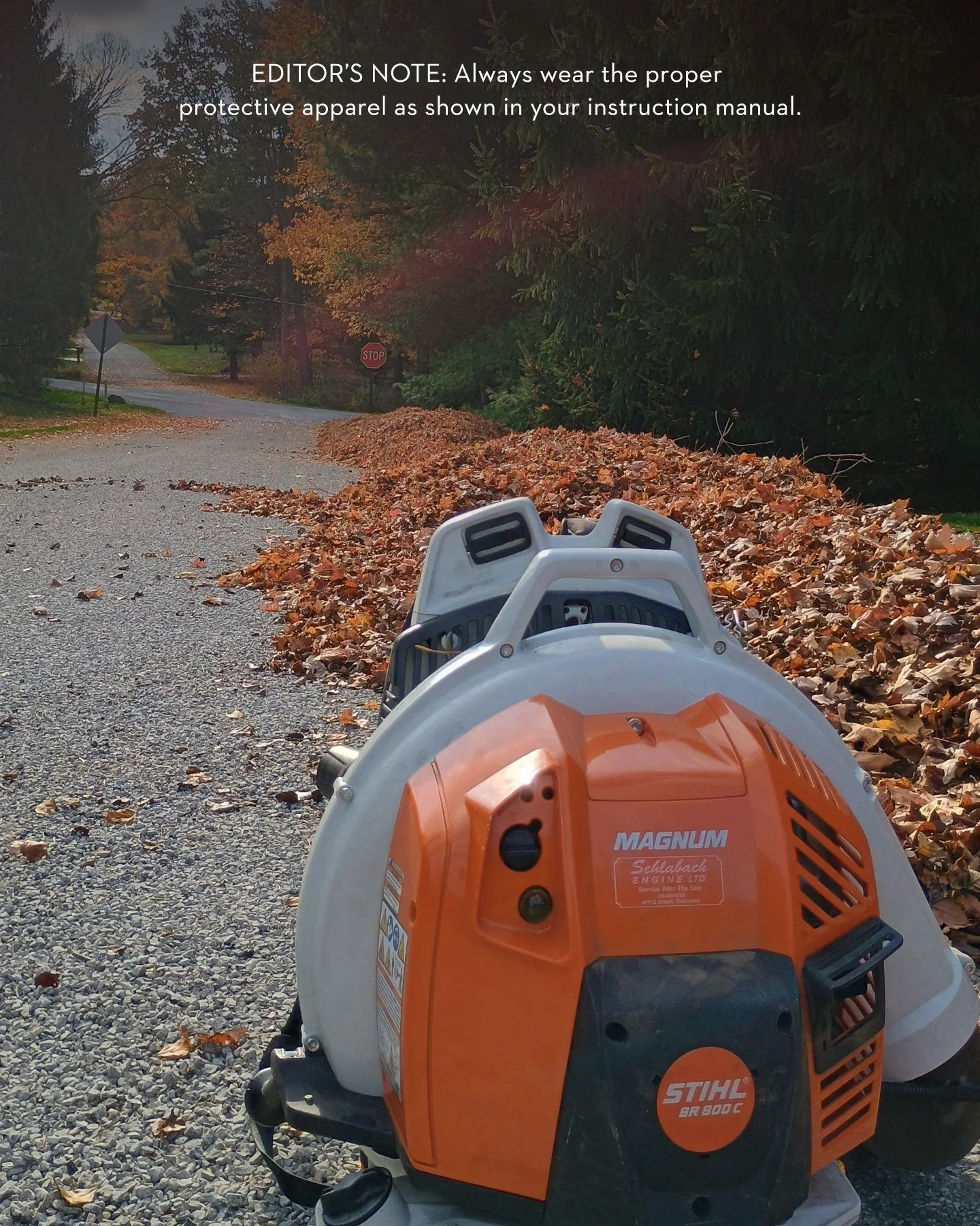 Orange and white leaf blower on a gravel path, blowing leaves toward the trees.