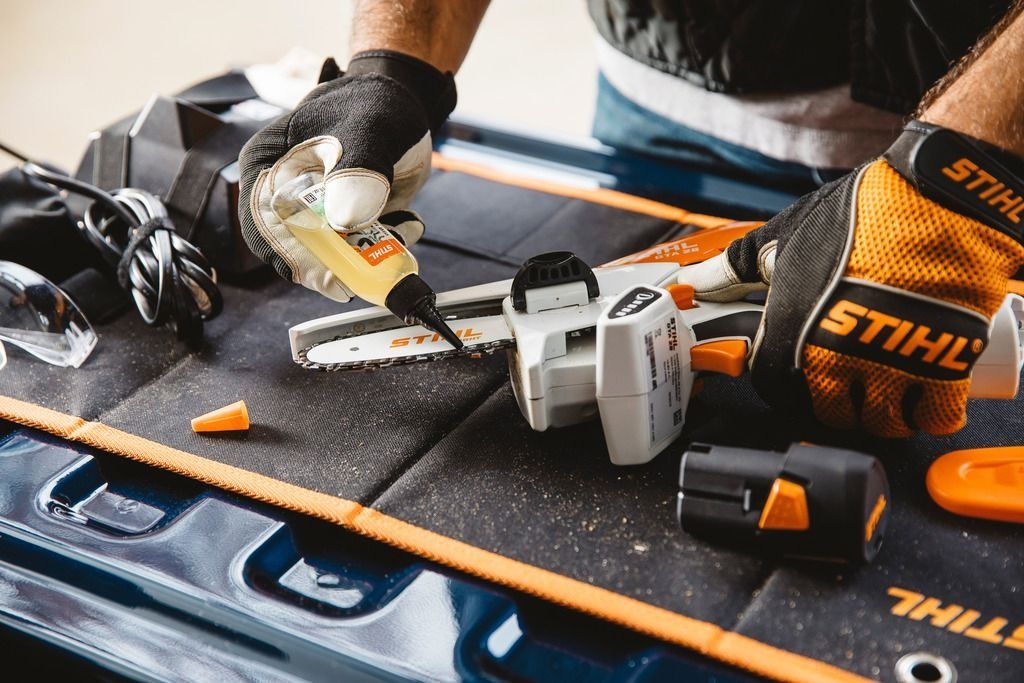 Person assembling a Stihl chainsaw with gloves, on a workbench. Black, orange, and white tools are visible.