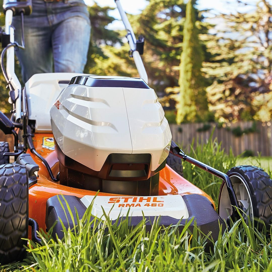 Person mowing lawn with orange and white Stihl lawnmower on a sunny day.