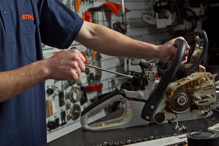 Person working on a chainsaw with a tool in a workshop.