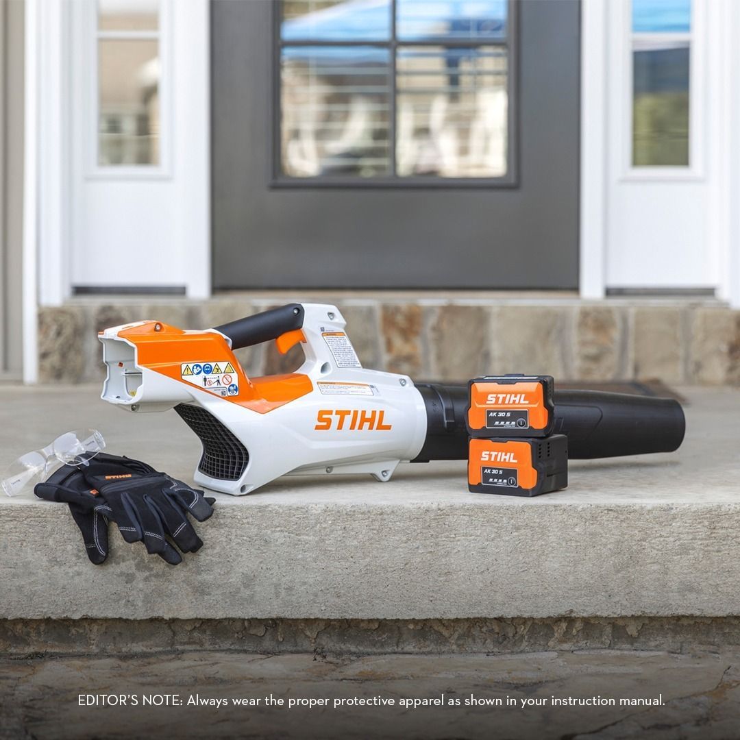 Battery-powered Stihl leaf blower with batteries, gloves, sitting on a porch.