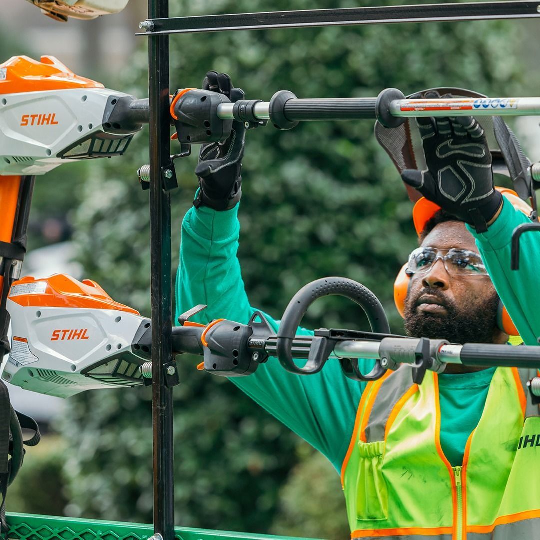 Man wearing safety gear adjusts a lawn tool on a rack.