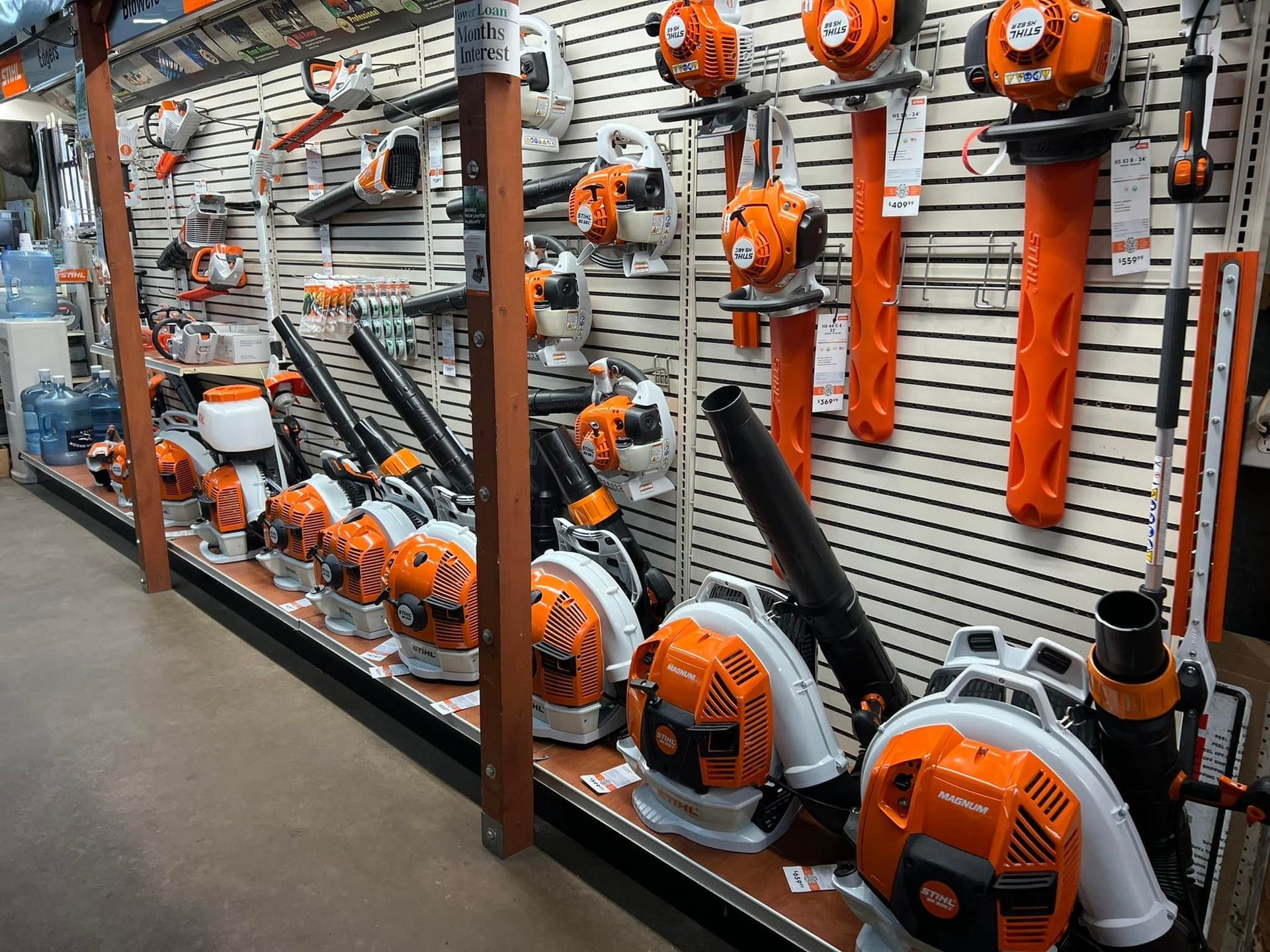 A store display featuring rows of orange and white leaf blowers on shelves and hanging on a slatwall.
