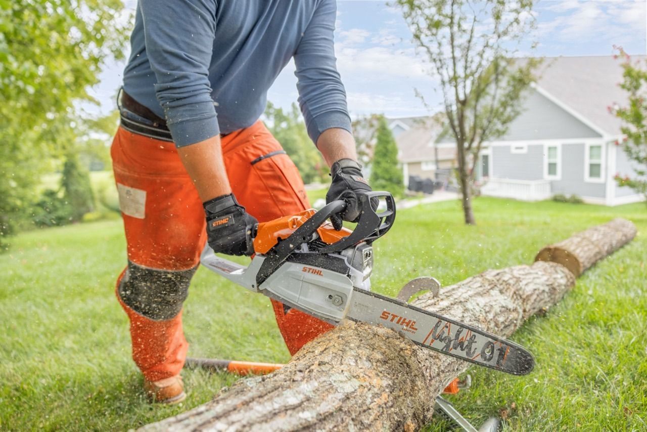 Person in orange pants using a chainsaw on a log in a yard.