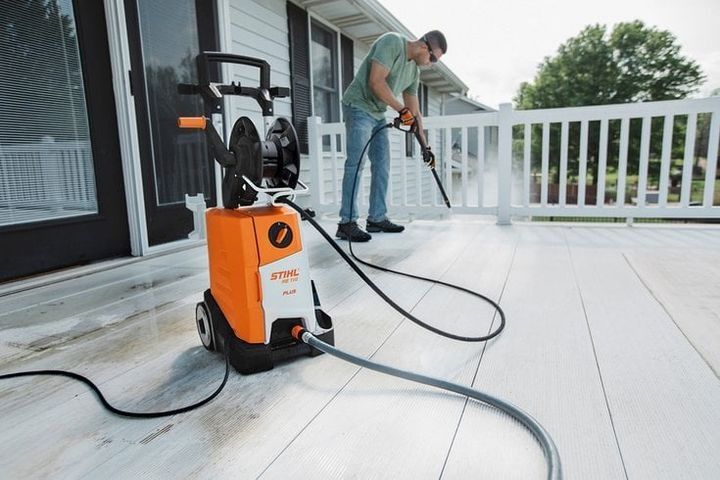 Man power washing a white wooden deck with a pressure washer.