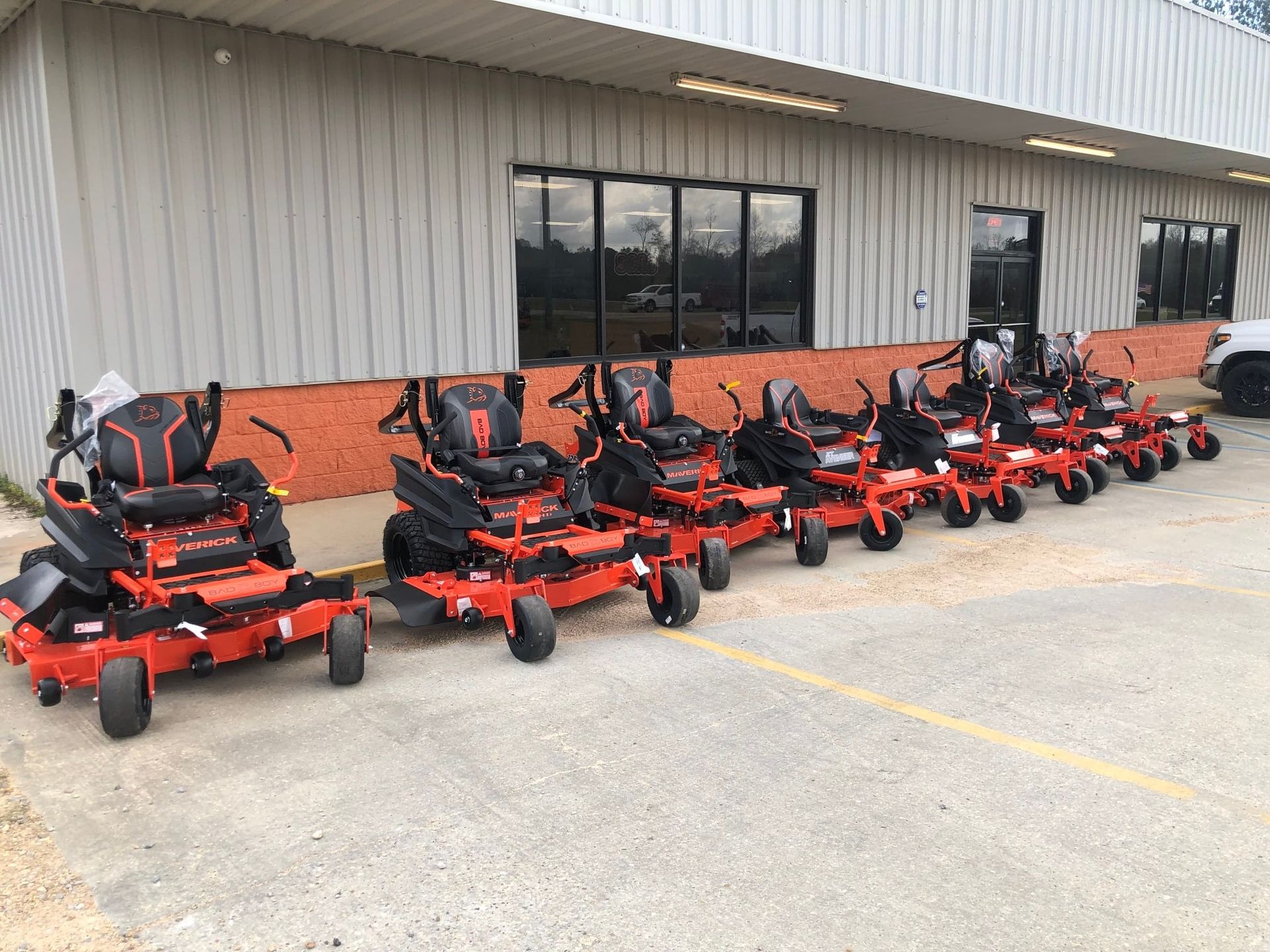 Lineup of red zero-turn mowers parked in front of a building.