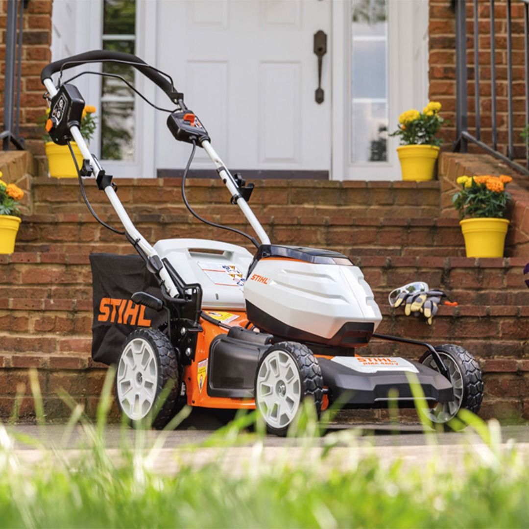A Stihl electric lawnmower on brick steps in front of a white door with yellow flower pots.