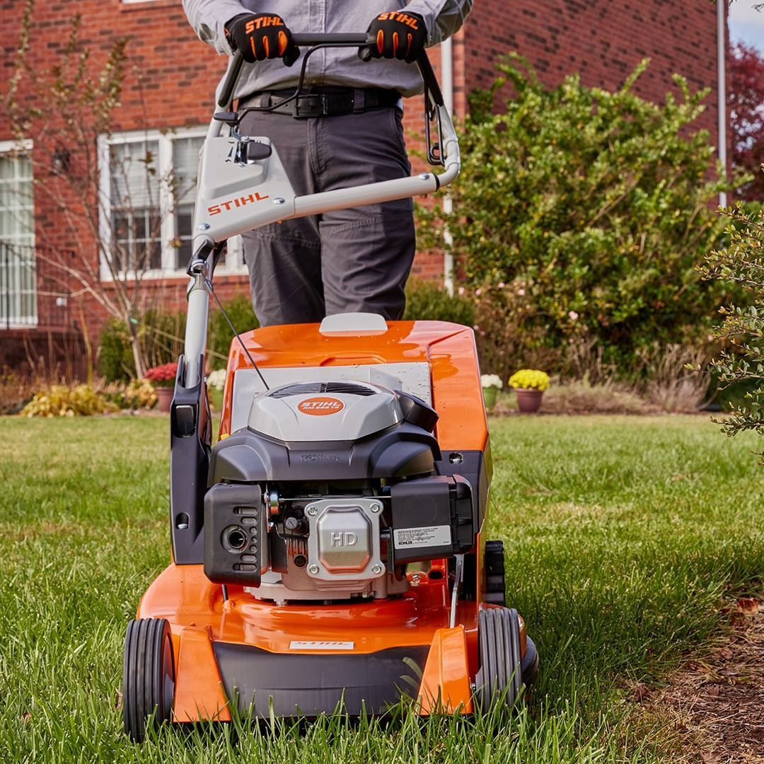 Person operating a bright orange lawnmower on a grassy yard in front of a house.