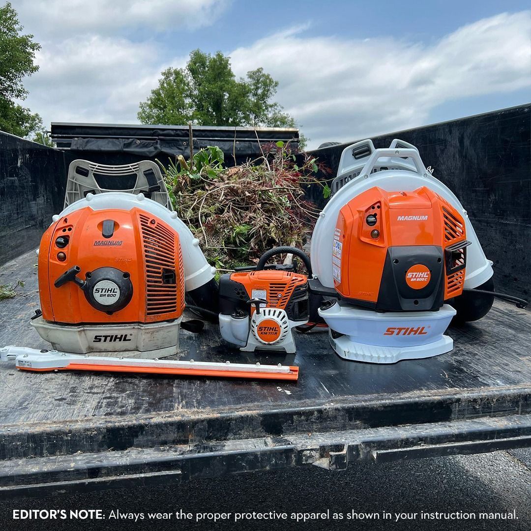 Three Stihl leaf blowers sit in the back of a truck, ready to use on a pile of yard debris.
