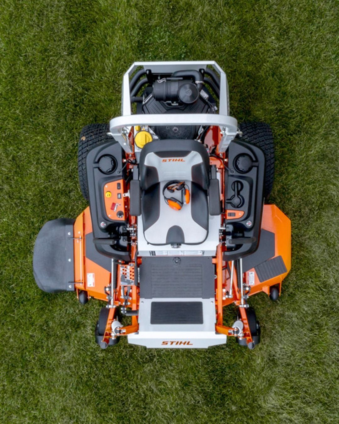 Overhead view of an orange and white zero-turn lawn mower on green grass.