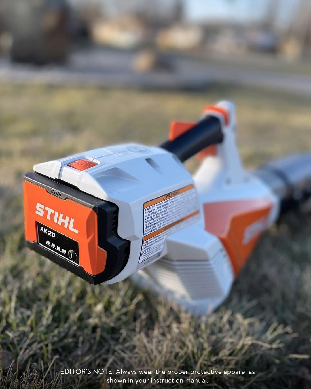 White and orange Stihl battery-powered leaf blower on grass, battery indicator lit.