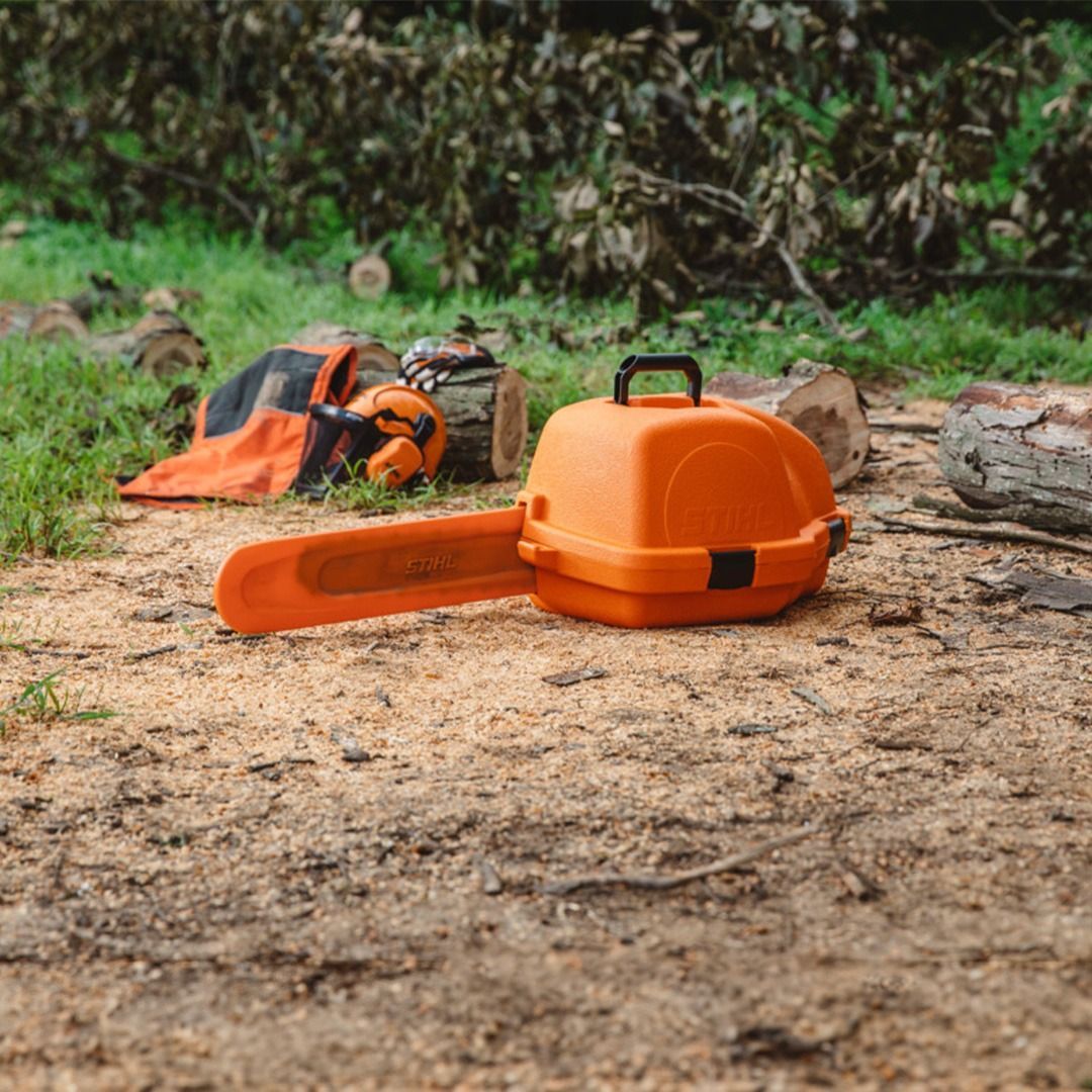 Orange chainsaw case on sawdust, with chainsaw bar extended. Safety gear in background.