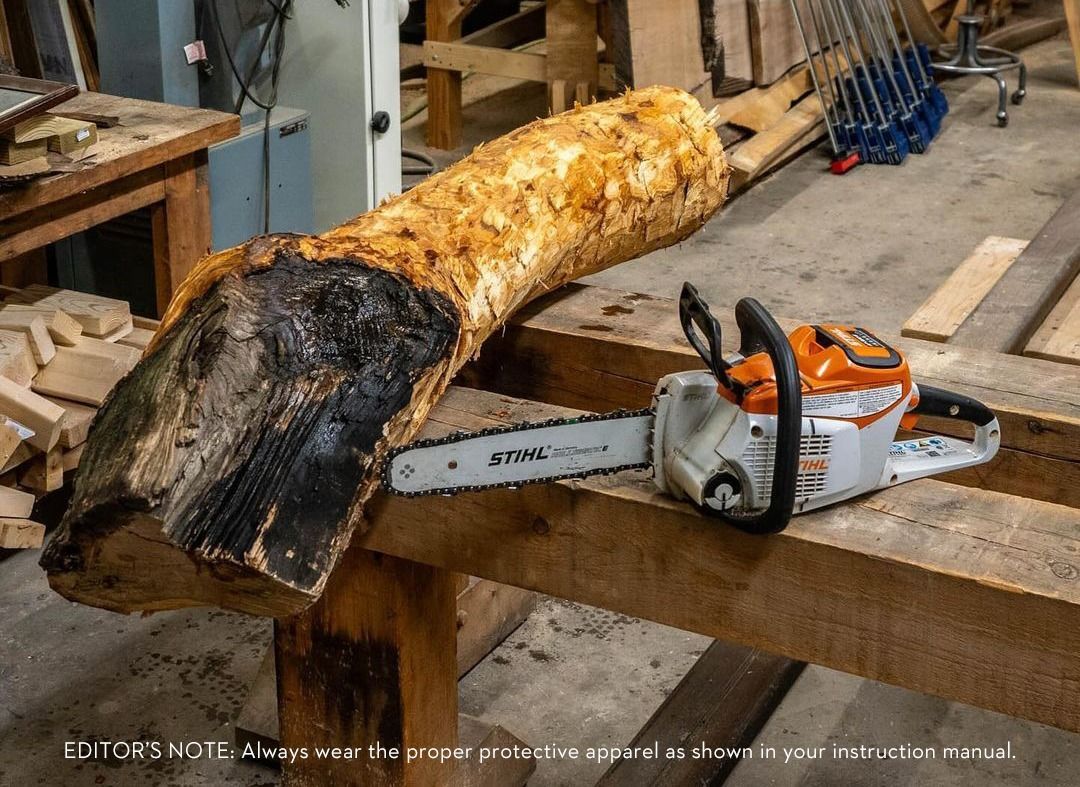 A chainsaw next to a charred log on a wooden workbench.
