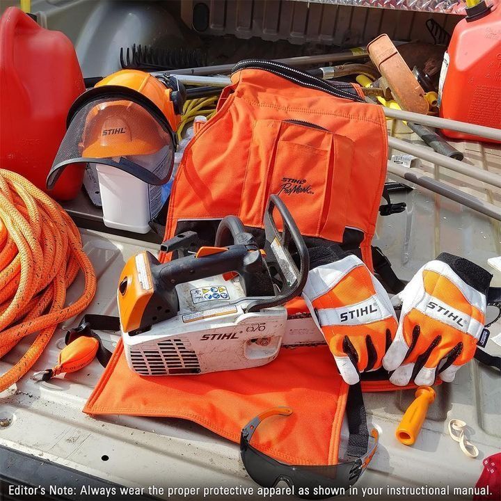 Orange chainsaw and protective gear (gloves, helmet, vest) in truck bed.