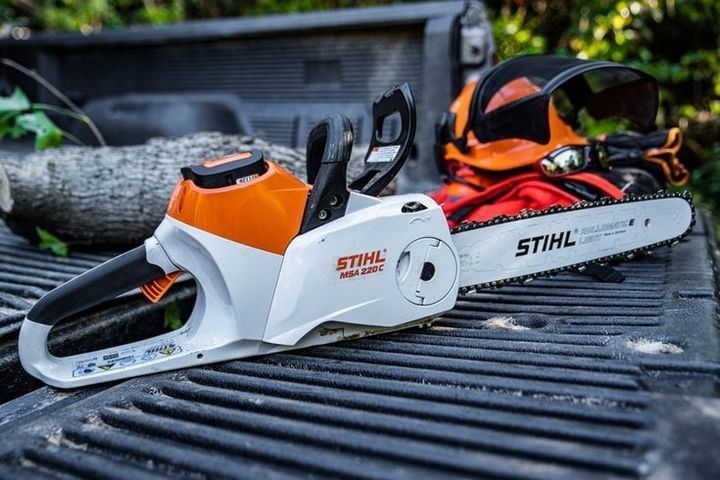 White and orange STIHL chainsaw on a truck bed, safety gear visible.
