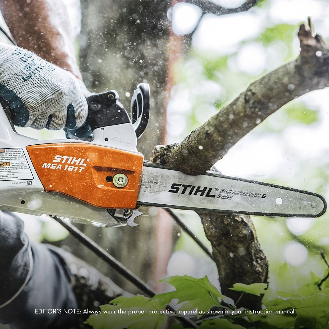 Person using a STIHL MSA 161 T chainsaw to cut a tree branch; white and orange saw, flying wood chips.