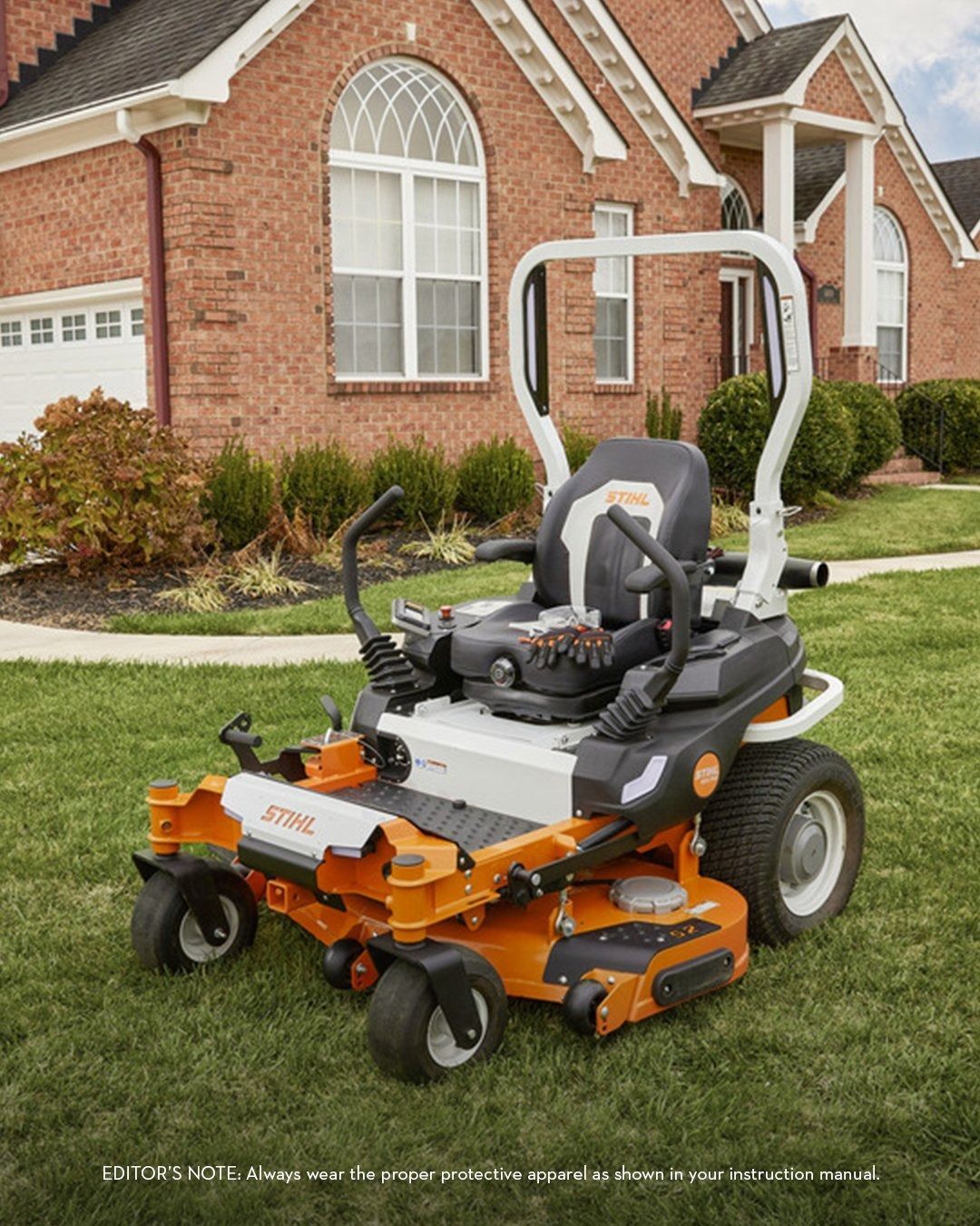 Orange and white zero-turn lawnmower on a green lawn in front of a brick house.