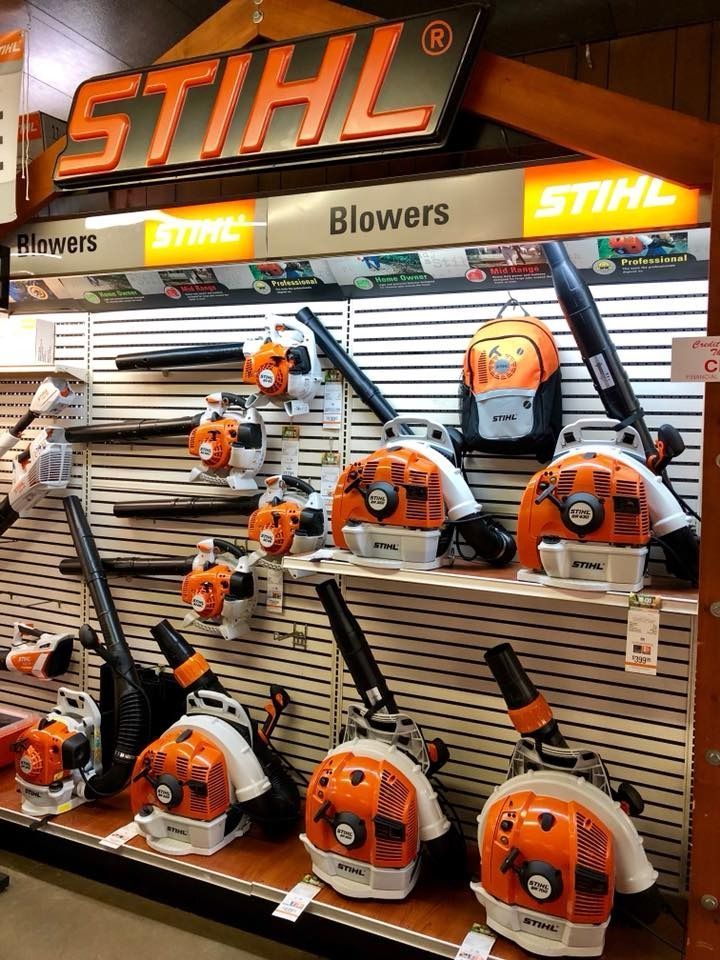 Stihl blowers displayed in a store. Orange and white blowers on shelves with a Stihl sign above.