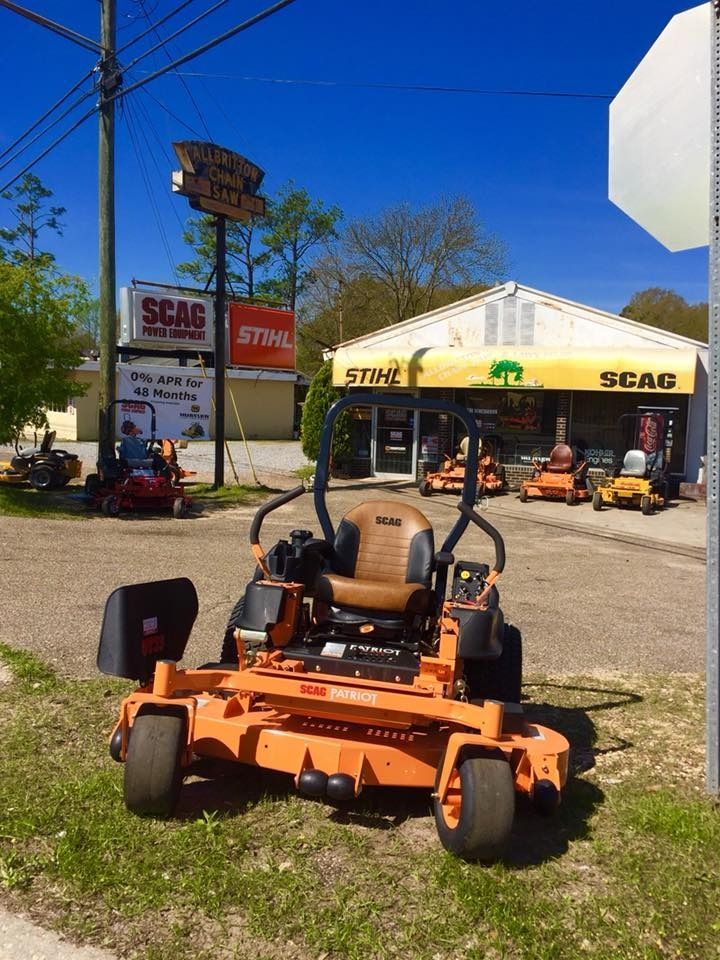 An orange Scag zero-turn mower in front of a lawn equipment store under a blue sky.