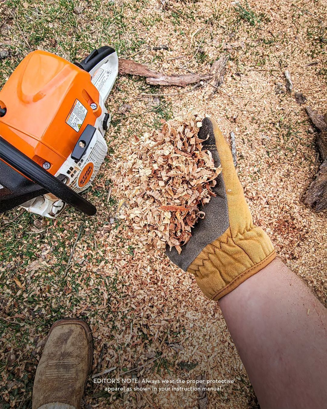 Person holding wood shavings next to a chainsaw and work boot on the ground.