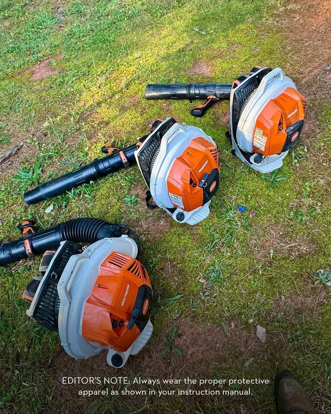 Three orange and gray backpack leaf blowers on green grass.