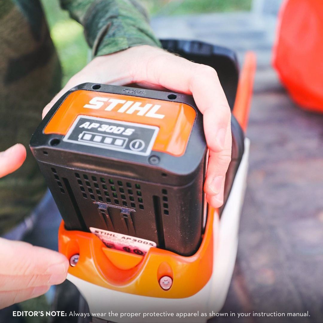 Person inserts a Stihl AP 300 S battery into an orange and white lawn tool.