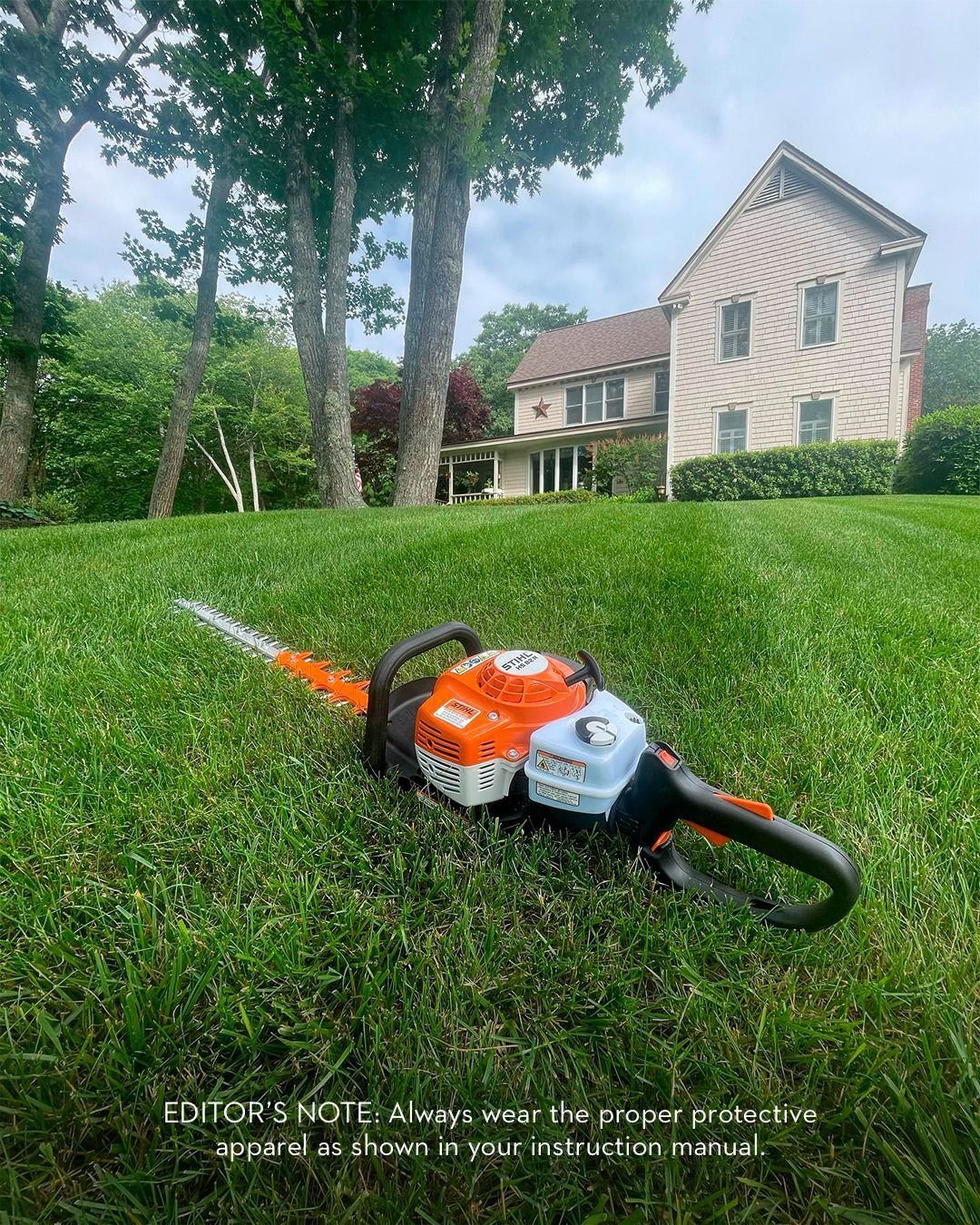 Orange and white hedge trimmer on a grassy lawn with a house in the background.