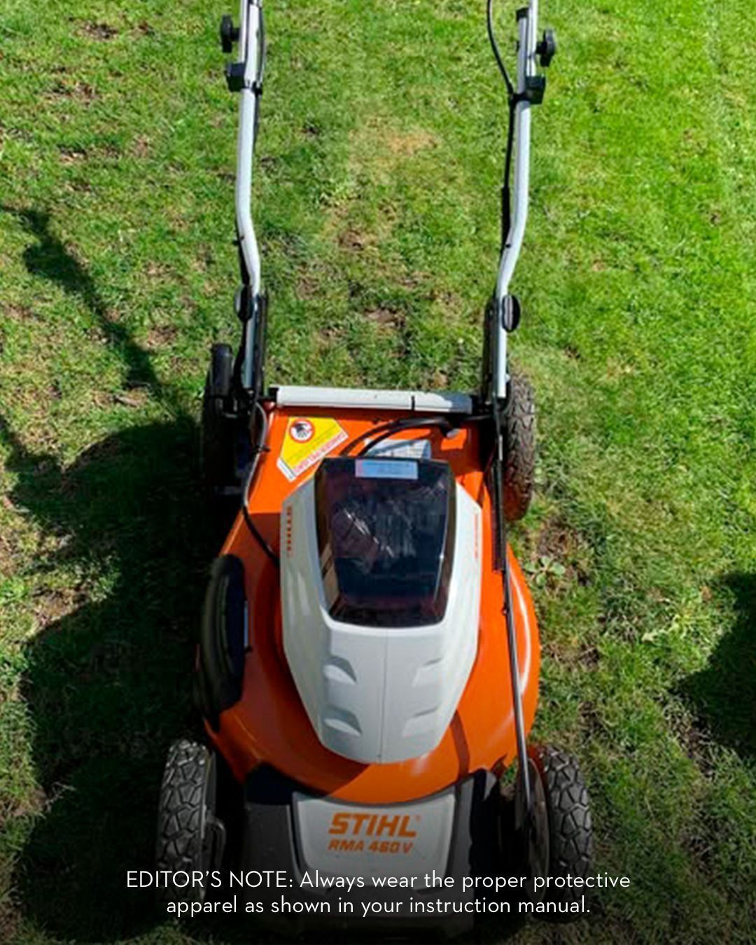 Orange and white Stihl battery-powered lawn mower on grass, handles raised.