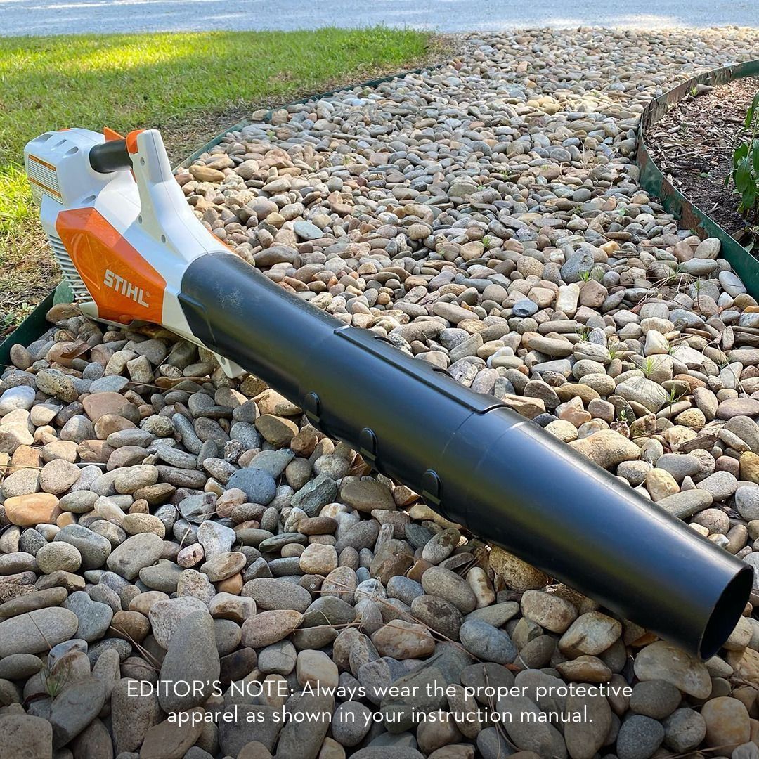 A Stihl leaf blower resting on a bed of rocks. The blower is white, orange, and black.