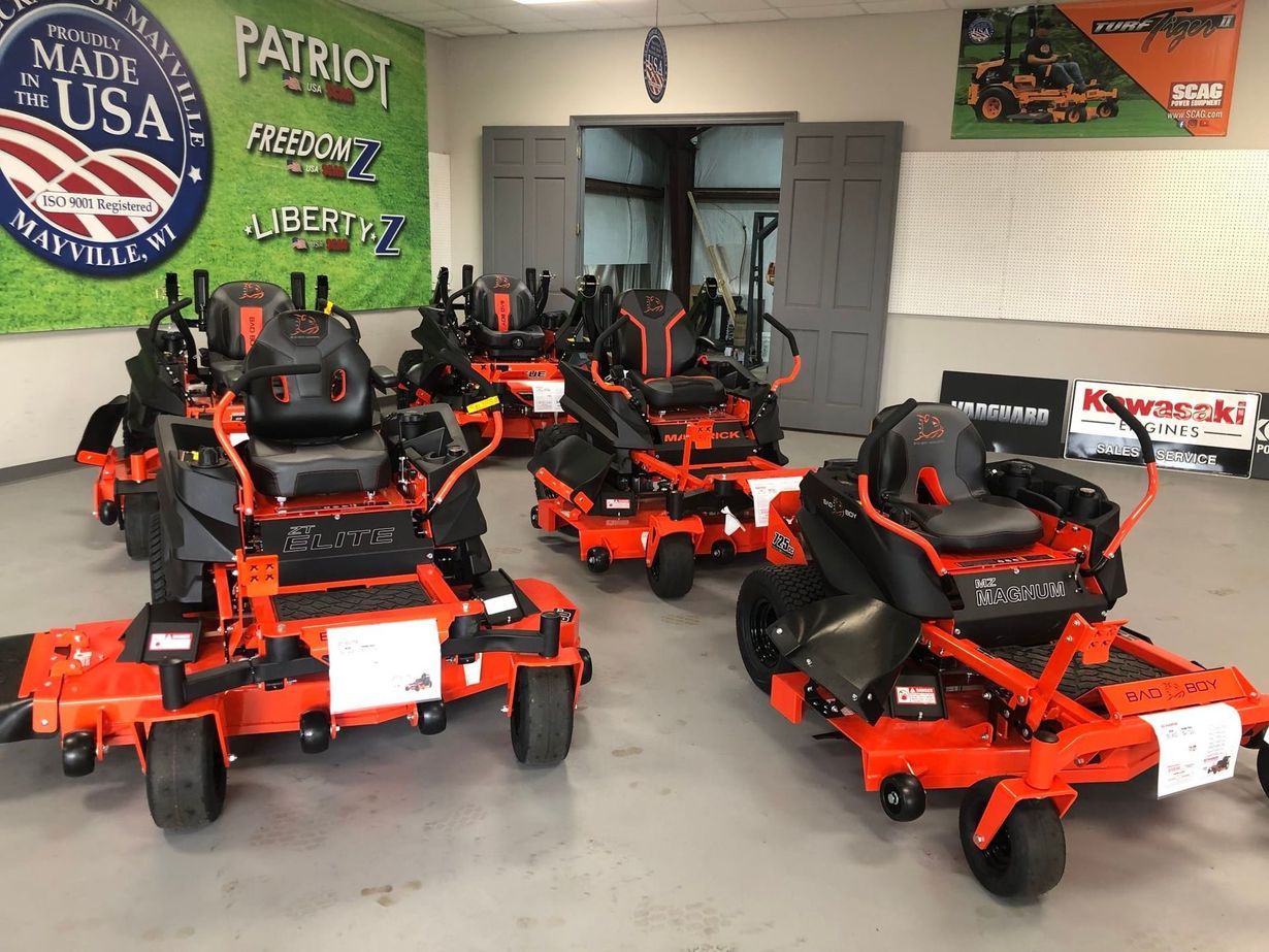 Orange and black zero-turn lawn mowers displayed inside a store with Patriot flag in background.
