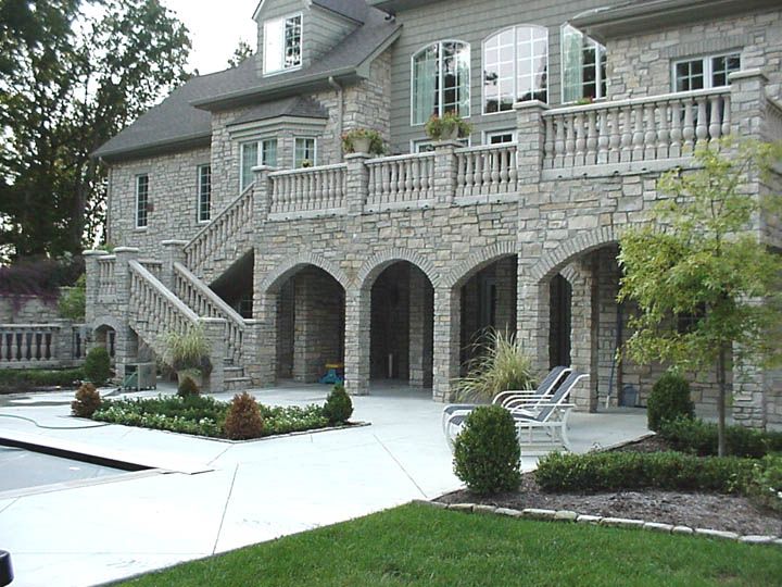 Stone house with arched garage doors, white stair railings, and a paved front driveway.