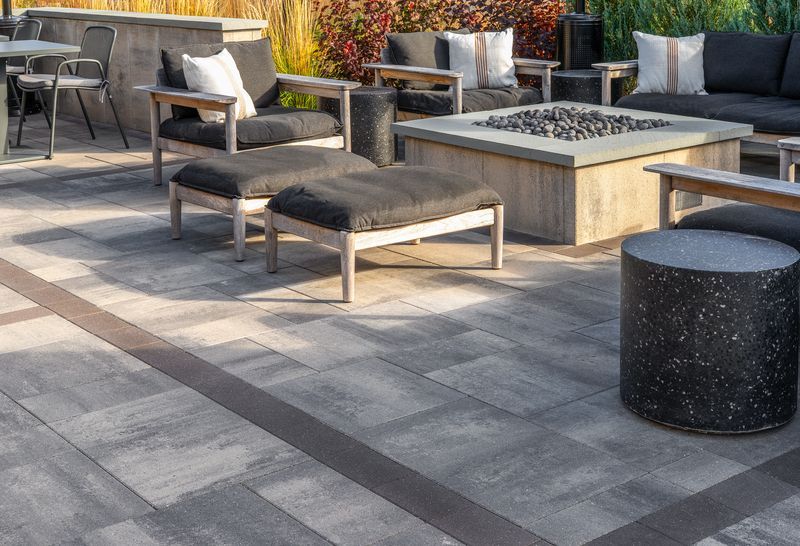 Outdoor patio seating area with gray lounge chairs, fire pit table, and stone pavers