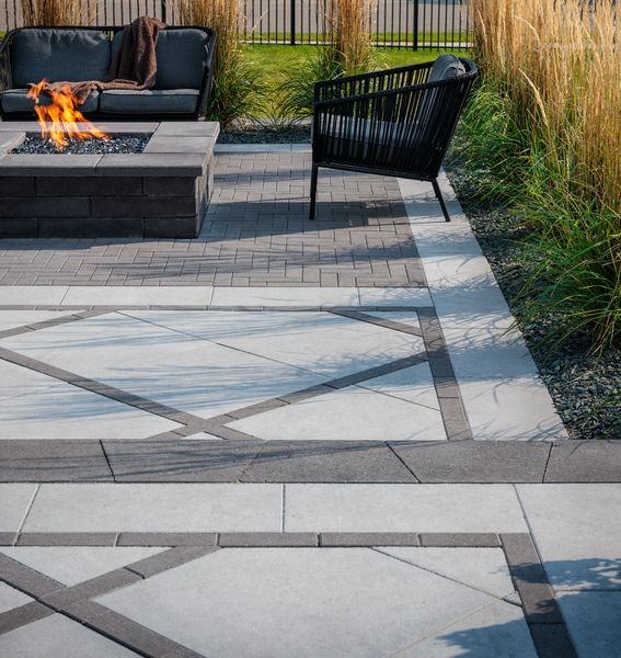 Modern patio with fire pit, black chairs, and patterned stone pavers beside tall grasses