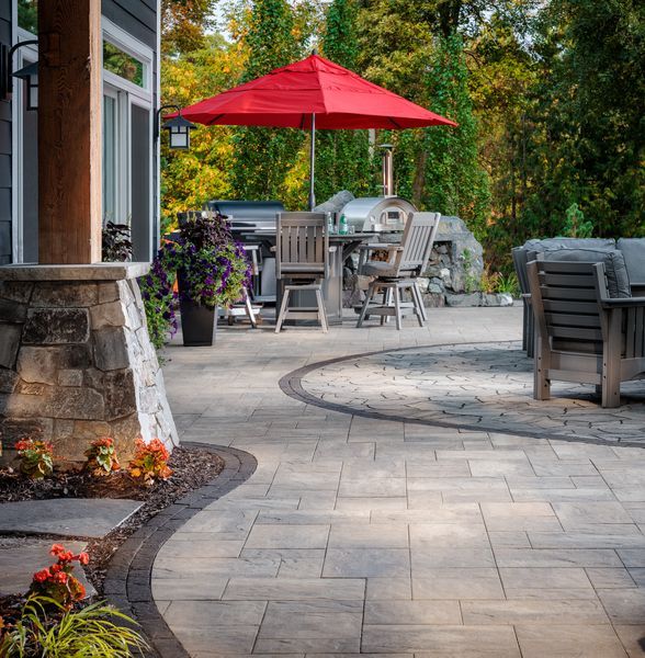 Patio with stone pavers, outdoor tables and chairs, and a red umbrella in a garden setting