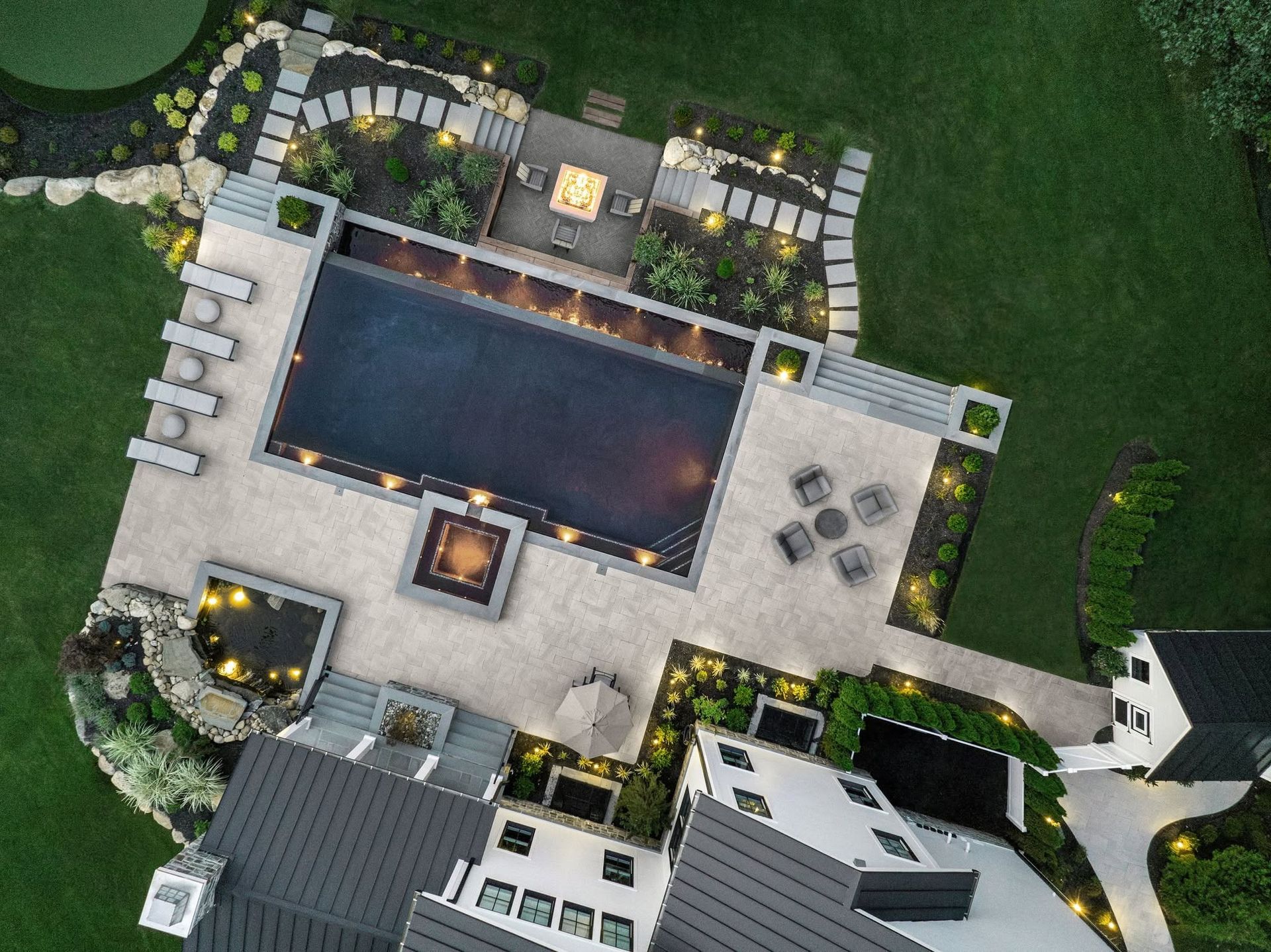 Aerial view of a modern rooftop pool deck with loungers, seating areas, and surrounding greenery.
