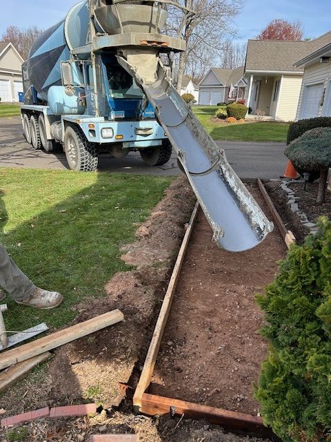 Concrete truck pouring cement into a formed walkway on a grassy residential lawn.