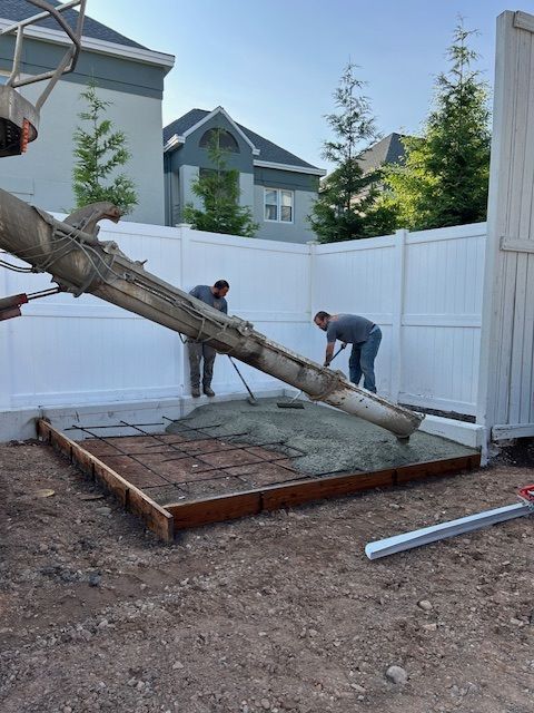 Two men are distributing concrete outside by white walls.